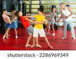 Positive kids in pair exercising self-defense movements during group class with male coach