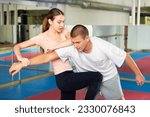 Young woman exercising knee strike on man during self-protection training.