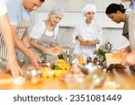 Small photo of Amiable young woman, qualified chef, running culinary courses for mixed age group of interested people, sharing secrets of cooking salmon steak..