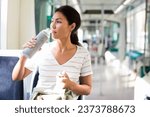 Asian woman sitting in tram with bottle of water in hand.