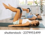 Motivated teenage girl maintaining active lifestyle exercising with ball during group workout in modern fitness center..