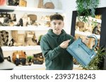 Small photo of Shocked appalled guy holding in hands stylish leather womens handbag and looking at price tag in trendy boutique..