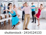 Small photo of Positive adult pairs practicing vigorous jive movements in dance class