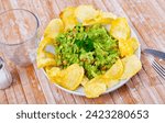 Small photo of On table in cafe there is plate with traditional Mexican snack guacamole and pile of crispy potato chips. Salty and savory light repast for beer