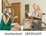 Positive female friend visiting disabled woman on chair indoor