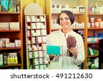Small photo of friendly smiling mature woman in white coat standing with bunch of dried vulnerary herbs in drugstore