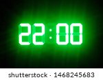 Green glowing digital clocks in the dark show 22:00 time