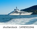 Huge luxury motor yacht cruising offshore in a calm ocean passing a forested coastline viewed over the wake of a passing ship