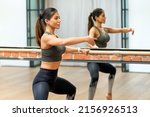 Small photo of Attractive fit woman performing plie squat exercises on a barre in a gym reflected in the wall mirror behind during booty barre class
