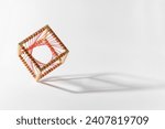 Small photo of Vivid display of unstable platonic solid wooden cube with red woven thread standing on edge against bright white background with shadow
