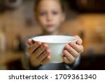Unrecognizable child girl reaching out hands holding white empty bowl plate offering food or asking for food. Shallow focus. Giving concept. Hungry children