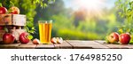 Apple Crate And Glass Of Juice On Wooden Table With Sunny Orchard Background - Autumn / Harvest Concept