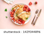 Crepes with ricotta cheese and fresh strawberries on pink pastel background, top view, copy space. Delicious crepes, thin pancakes.