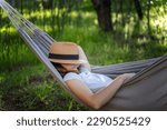 Woman resting in a hammock in a summer garden covering her face with a straw hat. Summer vacation concept