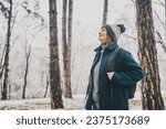 A young mature woman breathes fresh air and enjoys the snowfall in the winter forest. Winter walks and activity concept