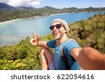 Young male hipster traveler doing selfie overlooking the tropical sea. Adventure, vacation, wonderlust, internet, technology concept.