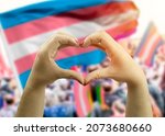 close up hands creating a heart with  transgender flag in the background