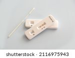 Two covid antigen rapid test kits and a nasal swab with positive results on white background, covid-19 lab testing concept