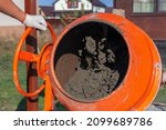 Small photo of Cement slurry in an orange concrete mixer on a sunny summer day