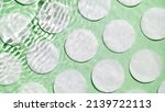 Small photo of Multiple waves of water create ripples spontaneously on green background with cotton pads | Background shot for face lotion commercial