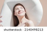 Small photo of The sun comes out and young good-looking European brown-haired woman looks upward enjoying it and smiling for the camera against beige background | Sunscreen wearing shot for face care commercial