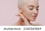 Small photo of Beautiful young slim Caucasian woman with fair hair strokes her jawline looking away on pale pink background | Sagging jowls removal concept