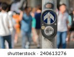 Pedestrian button at a pedestrian crossing with blurred pedestrians in the background.