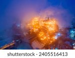 Small photo of Aerial view of metallurgical plant blast furnace at night with smokestacks and fire blazing out of the pipe. Industrial panoramic landmark with blast furnance of metallurgical production