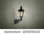 Vintage iron lantern hanging on concrete wall in evening time. Old lamp illuminating urban street.