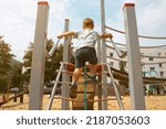 A child climbs up on a grid in park on a playground on a hot summer day. children's playground in a public park, entertainment and recreation for children, mountaineering training.