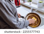 woman's hand washes burnt greasy frying pan with kitchen washcloth in sink. Dirty dishes with burnt food, household chores, washing dishes
