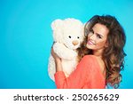 Lovely smiling young woman in knitted clothes holding big soft teddy bear on isolated blue background