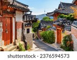 Small photo of Gorgeous view of cozy old narrow street and traditional Korean houses of Bukchon Hanok Village in Seoul, South Korea. Seoul Tower on Namsan Mountain is visible on blue sky background. Scenic cityscape