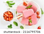 Strawberry ice cream popsicles on white plate. Top view, flat lay