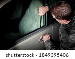 A male car thief uses a flat metal lock pick to break into a vehicle.