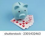 Blue piggy bank and hearts playing cards on blue background. 