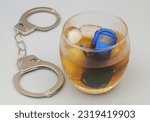 Small photo of Handcuffs with car model drowned in whisky glass on gray background.