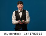 Small photo of Noob in poker, in black vest and trousers, white shirt. Holding some colored chips. Posing against blue background. Gambling, casino. Close-up.