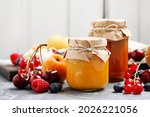 Two jars with peach jam and fresh fruits on stone background. 