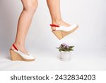 Small photo of female feet trample a flowerpot of violets on a light background