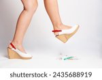Small photo of female feet trample syringes and medicines on a light background