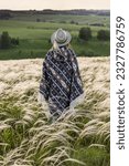 Small photo of Summer landscape, feather grass field, sky with clouds. A woman in a hat and a Peruvian poncho, seen from the back.