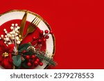 Christmas dinner concept. Top view of golden cutlery and christmas ornaments on a red plate with space for text over red background . Christmas concept background