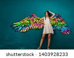 Smiling Caucasian girl in white summer dress posing in front of turquoise wall with colorful wings.