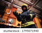 Closeup of fireman putting on gloves and preparing for action while standing in fire station.
