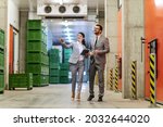 Small photo of Business people in the warehouse. A man and a woman dressed in a modern suit walk throw the warehouse and walk. A woman with a tablet in her hand showing the protocols in the warehouse
