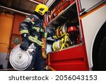 Small photo of Firefighter in protective uniform with helmet on head checking on hoses before intervention while standing in fire station.