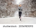 Full length of happy middle-aged sportswoman running in nature at snowy winter day. Outdoor fitness, cardio exercises, exercises in nature