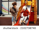 Small photo of A nanny babysitting a little boy at the playground. A woman encourages a little boy on the slides.