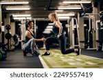 A female trainer is helping sportswoman to do exercises in a gym.